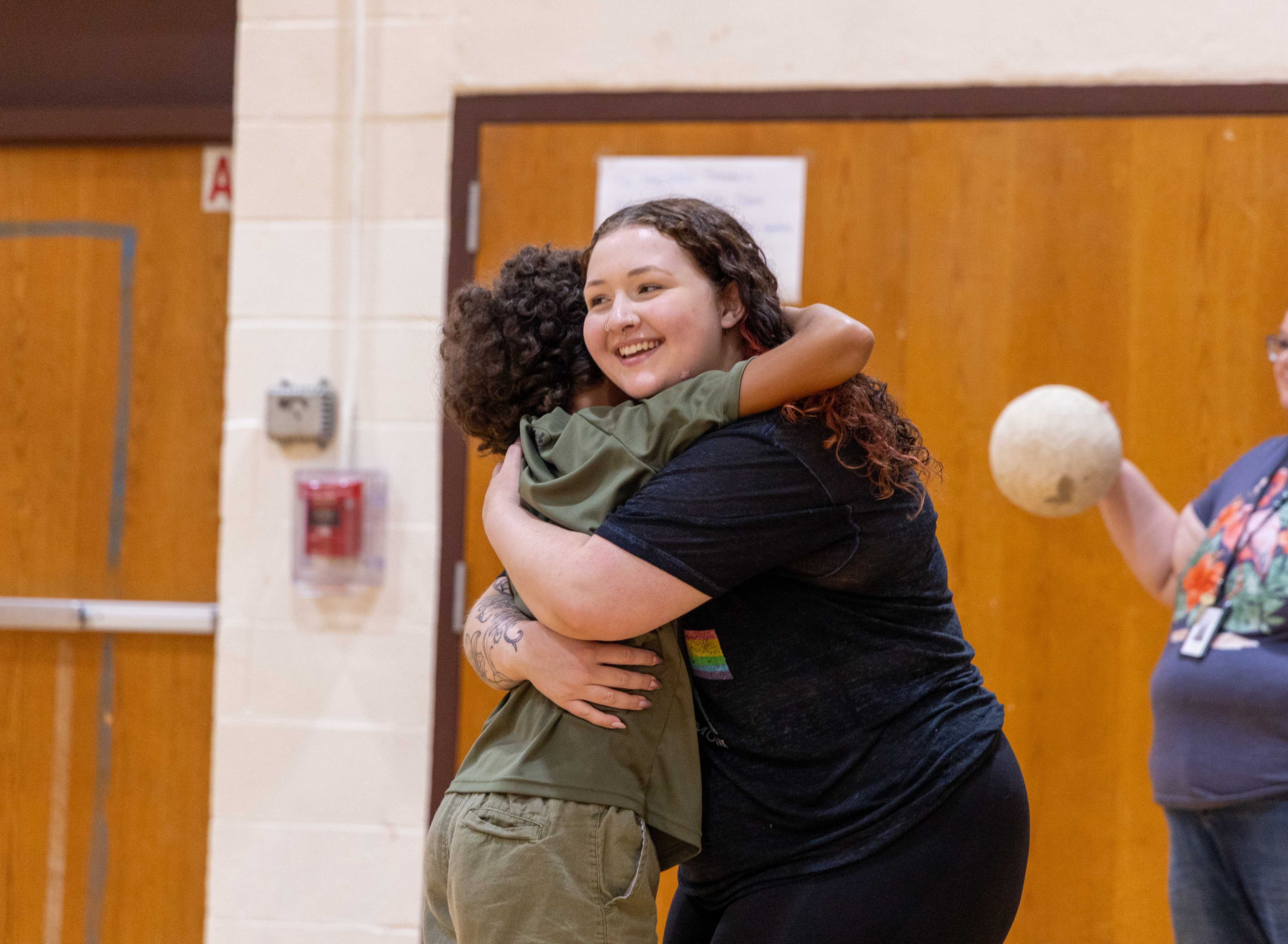 an aide hugs a young student, smiling